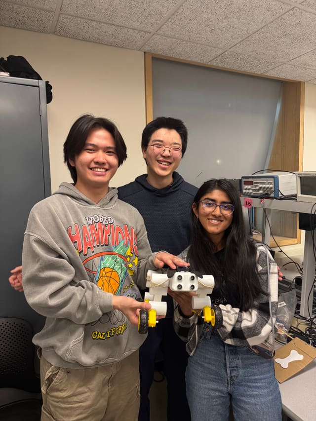 Shao and two teammates in the lab, holding the 3D-printed quadruped robot they built.