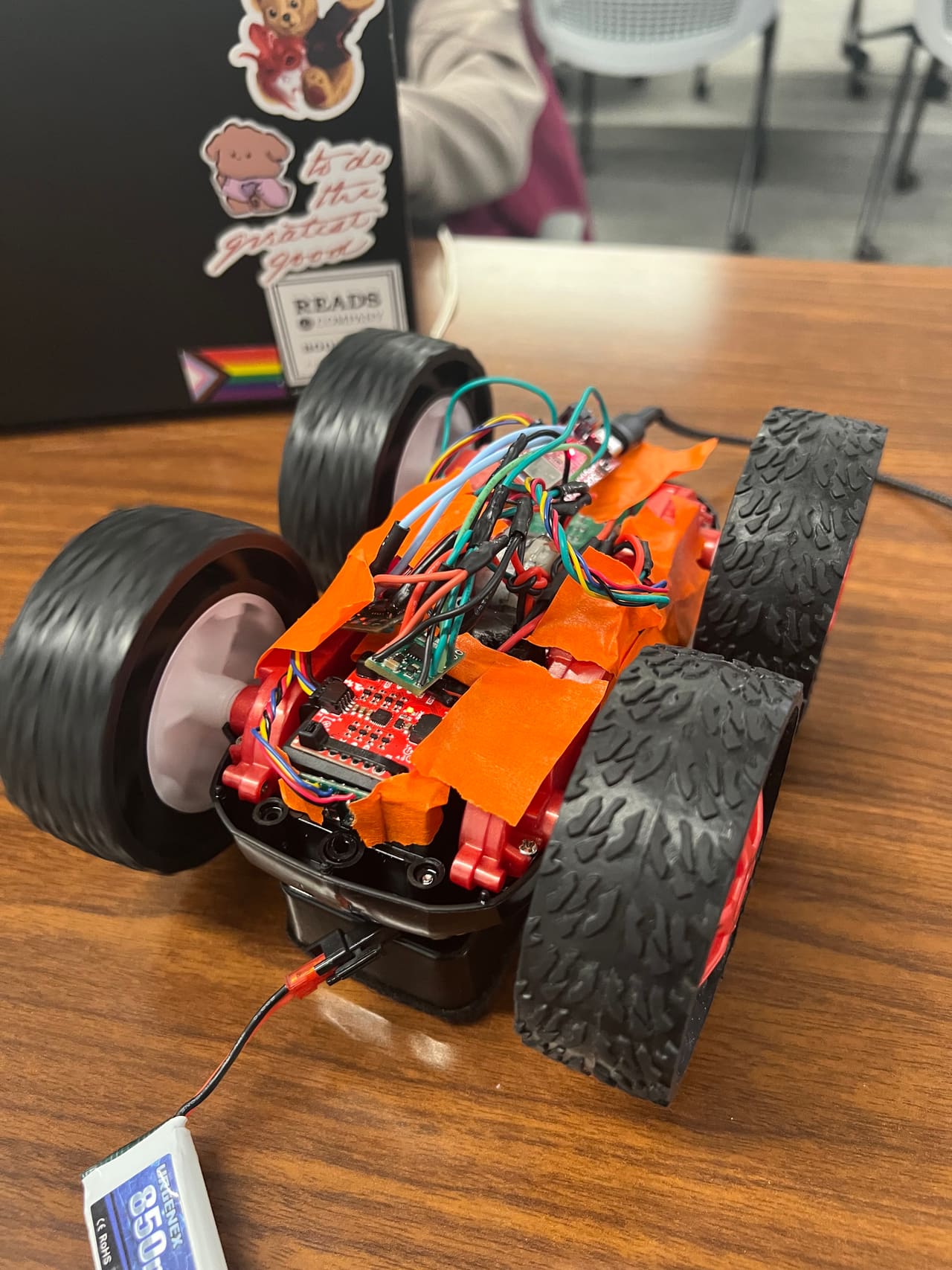 The Fast Robots car with its electronics exposed — control board, sensor wiring, and battery held down with orange tape.